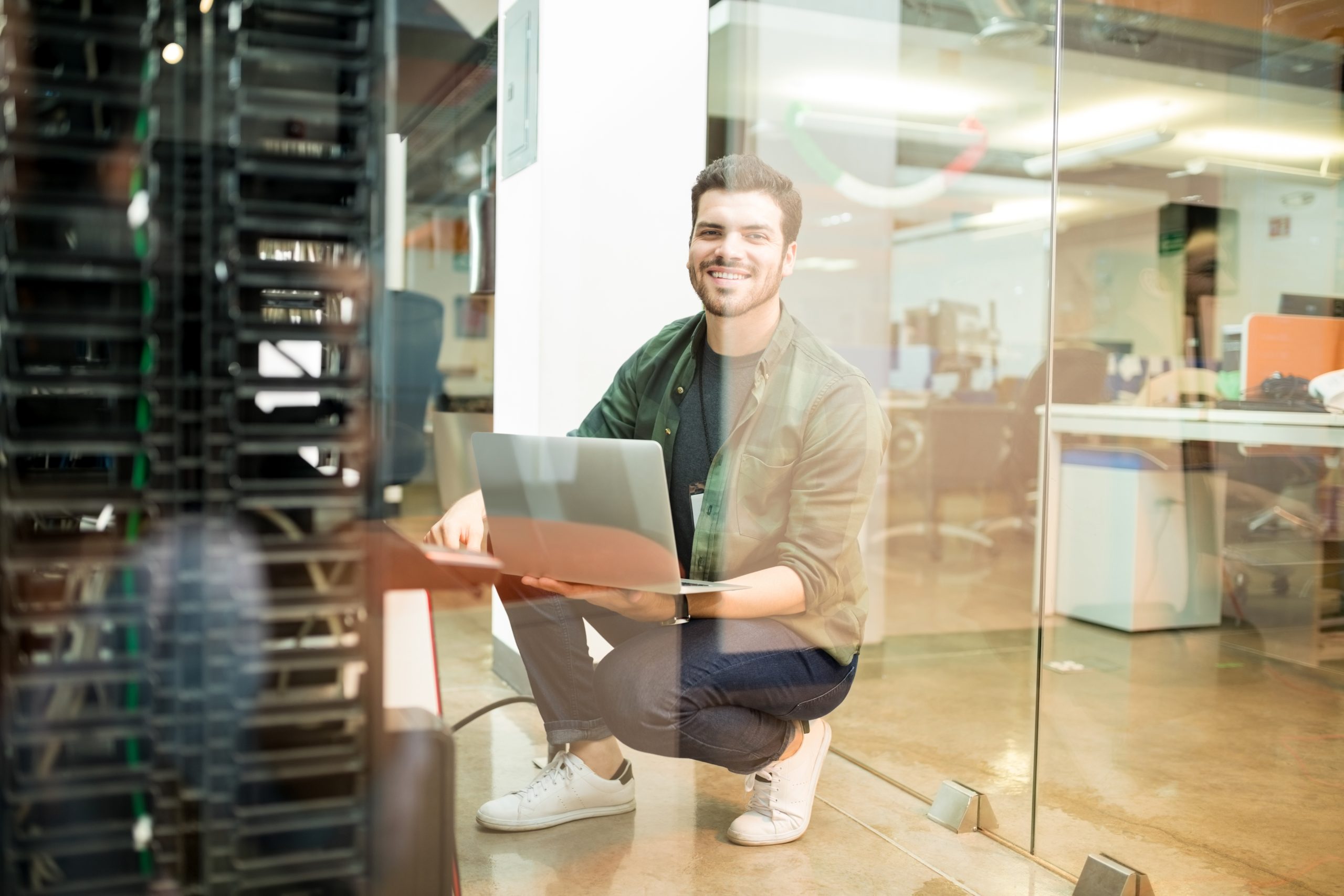 Portrait of happy young male network engineer with laptop in hand working in datacenter.